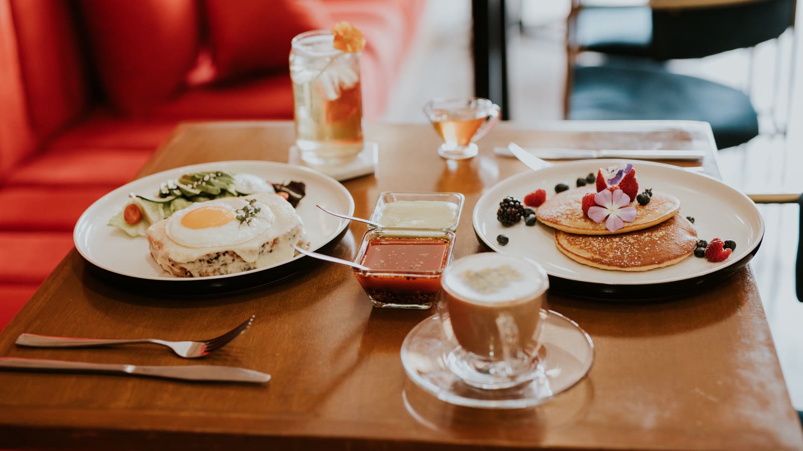 Brunchbord med to tallerkener: pandekager med friske bær og en spiselig blomst, og et varmt måltid med spejlæg, ved siden af kaffe og sirup