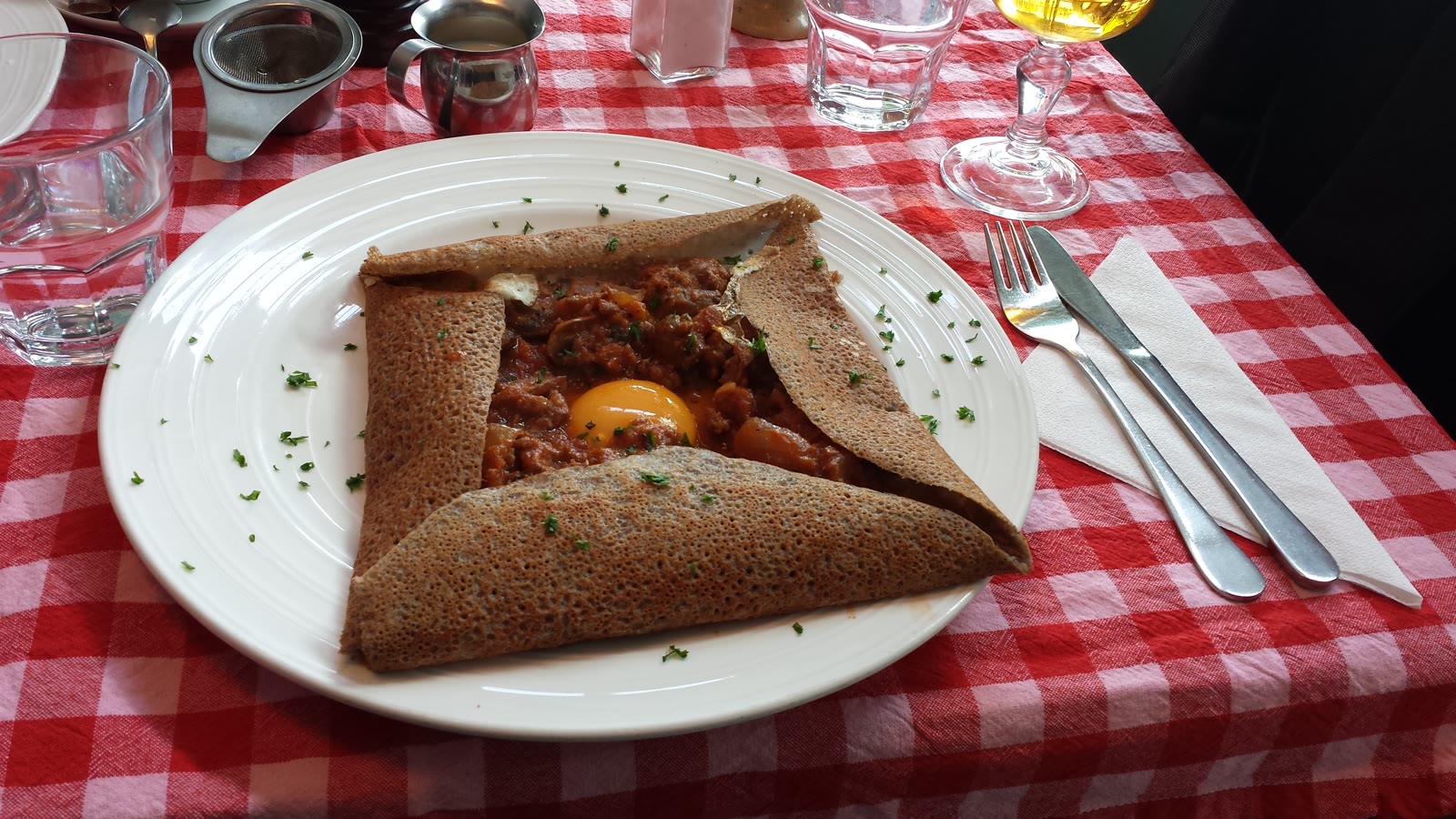 Bretonsk boghvedegalette foldet firkantet om æg og kødfyld, serveret på ternet dug