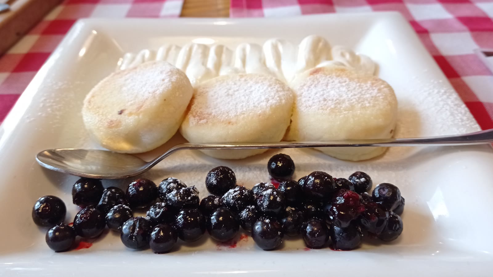 Tre tykke hytteostpandekager med flormelis, flødeskum og blåbær på en hvid tallerken